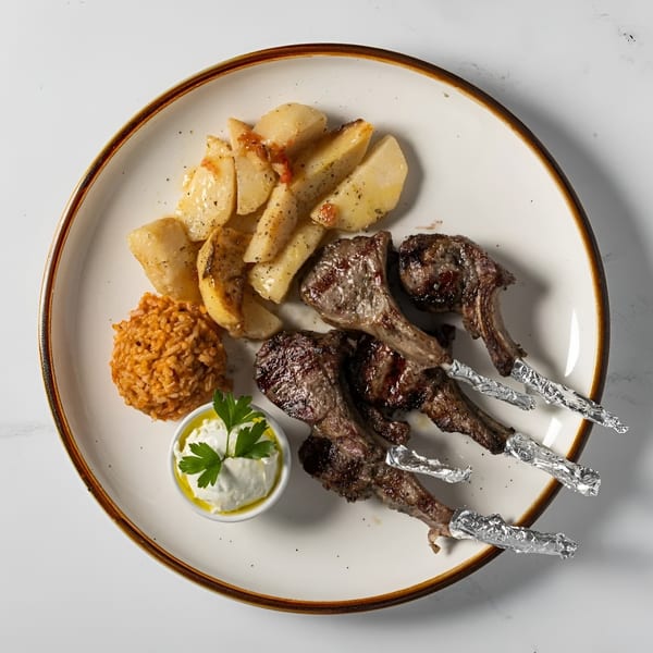 Grilled lamb chops with roasted potatoes, rice, and a side of tzatziki sauce.