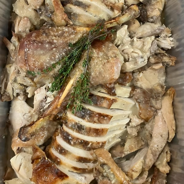 Roasted chicken pieces, some sliced, garnished with fresh herbs in a serving dish.