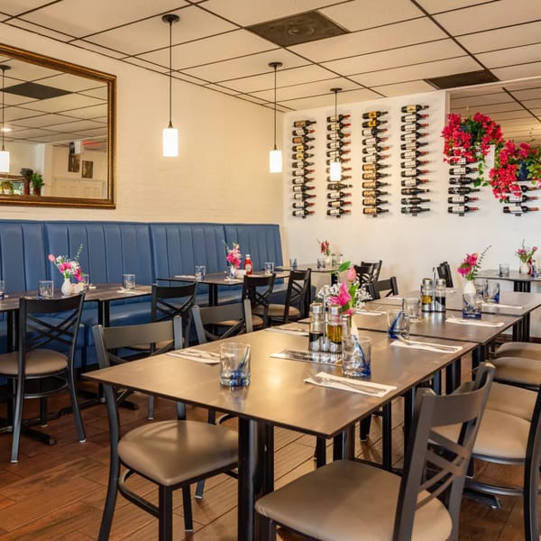 Djonisi's Restaurant dining room with blue booth seating, set tables, and wine bottles displayed on the wall.