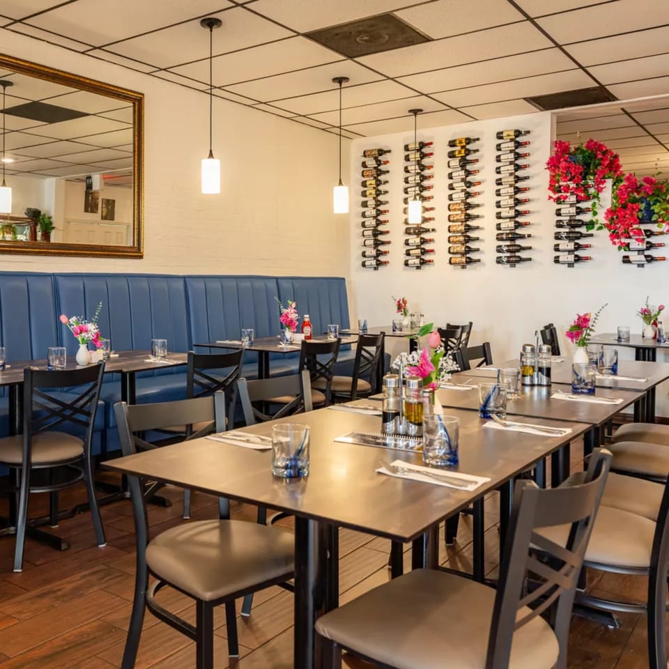 Djonisi's Restaurant dining room with blue booth seating, set tables, and wine bottles displayed on the wall.