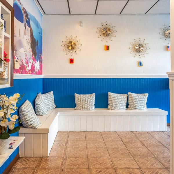 A white and blue waiting area with a mural of a Greek island and decorative clocks.