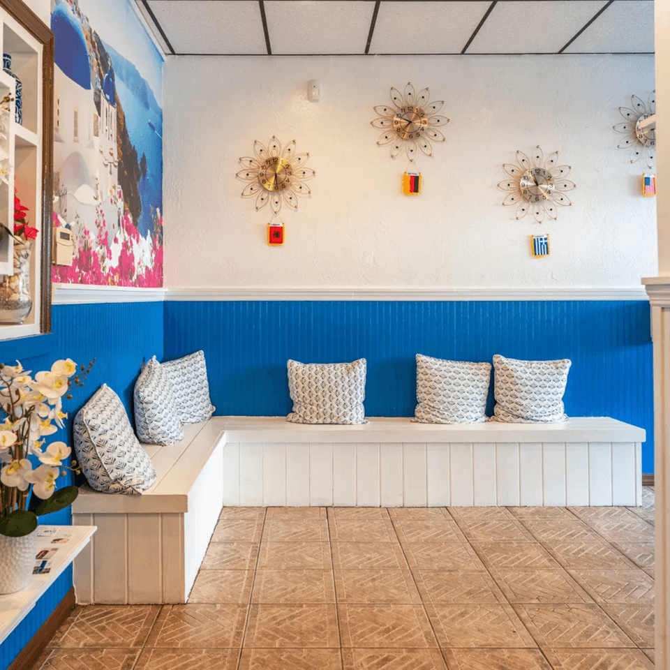 A white and blue waiting area with a mural of a Greek island and decorative clocks.