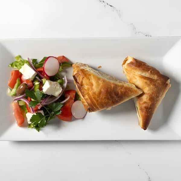 Two golden-brown Greek spanakopita pastries served with a fresh side salad on a white rectangular plate.
