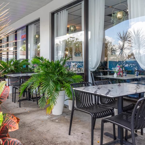 Outdoor patio seating at Djonisi’s Restaurant with marble tables, black chairs, and potted plants.