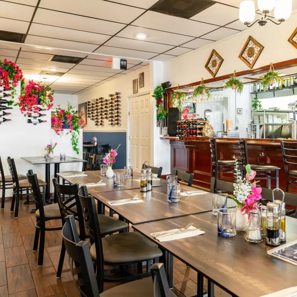 Interior of Djonisi’s Restaurant, showing dining tables, a bar, and wine racks with floral decorations.