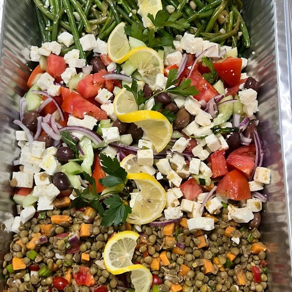 A catering tray with three Greek salads: green bean, feta with olives and tomatoes, and lentil.
